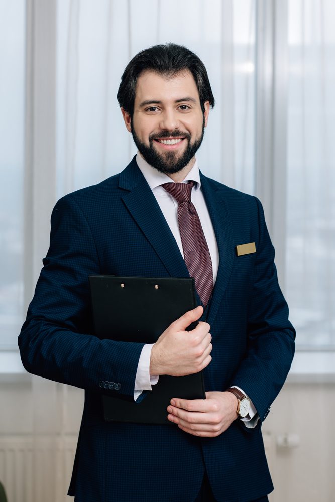 handsome hotel administrator with clipboard looking at camera